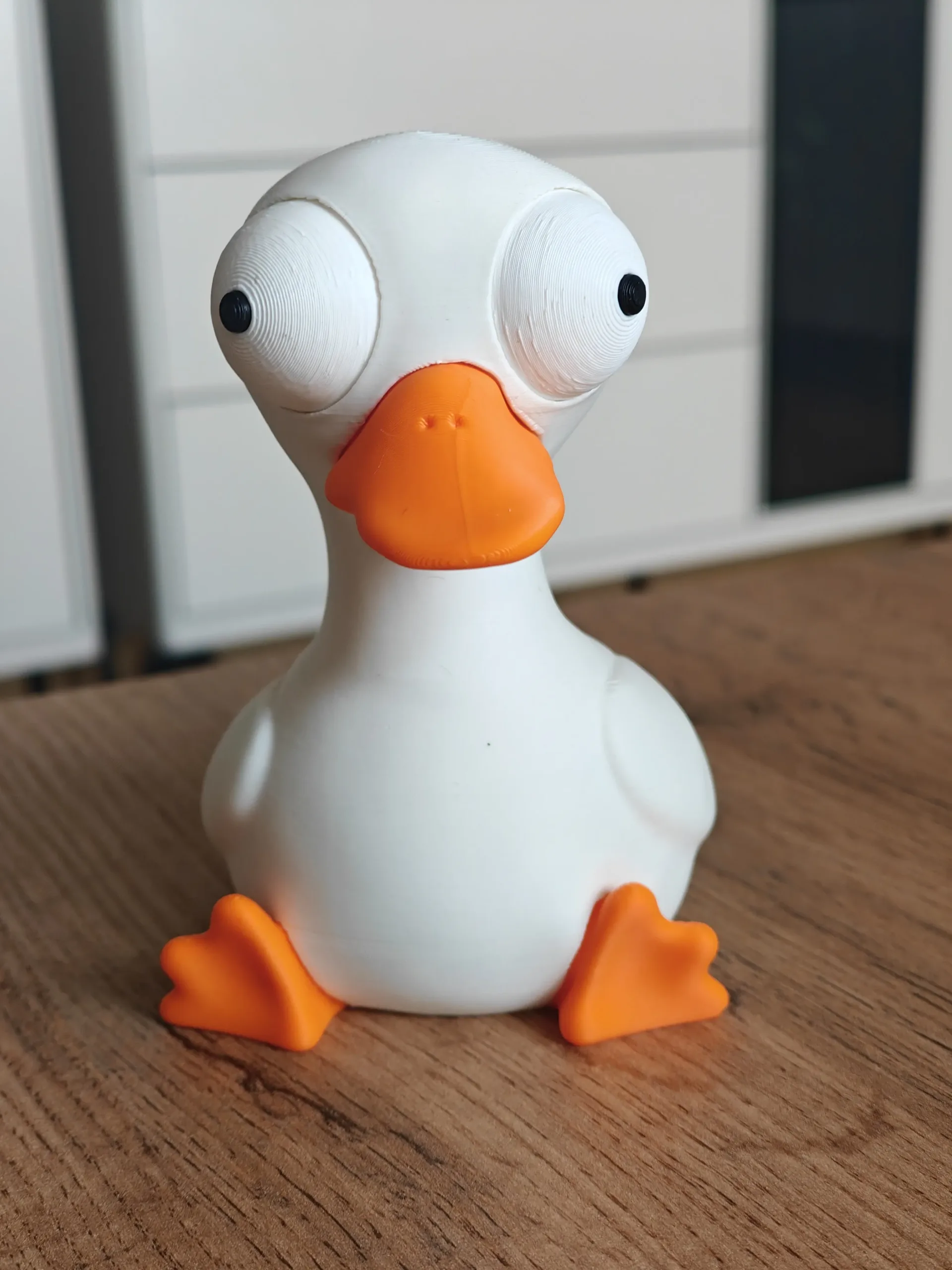 3D nyomtatott kacsa figura, cartoon / kawaii / quirky, dülledt szemű (bug-eyed), matt fehér test, narancs csőr és lábak – 3D nyomtatott dülledt szemű kacsa figura, háromnegyedes nézet
